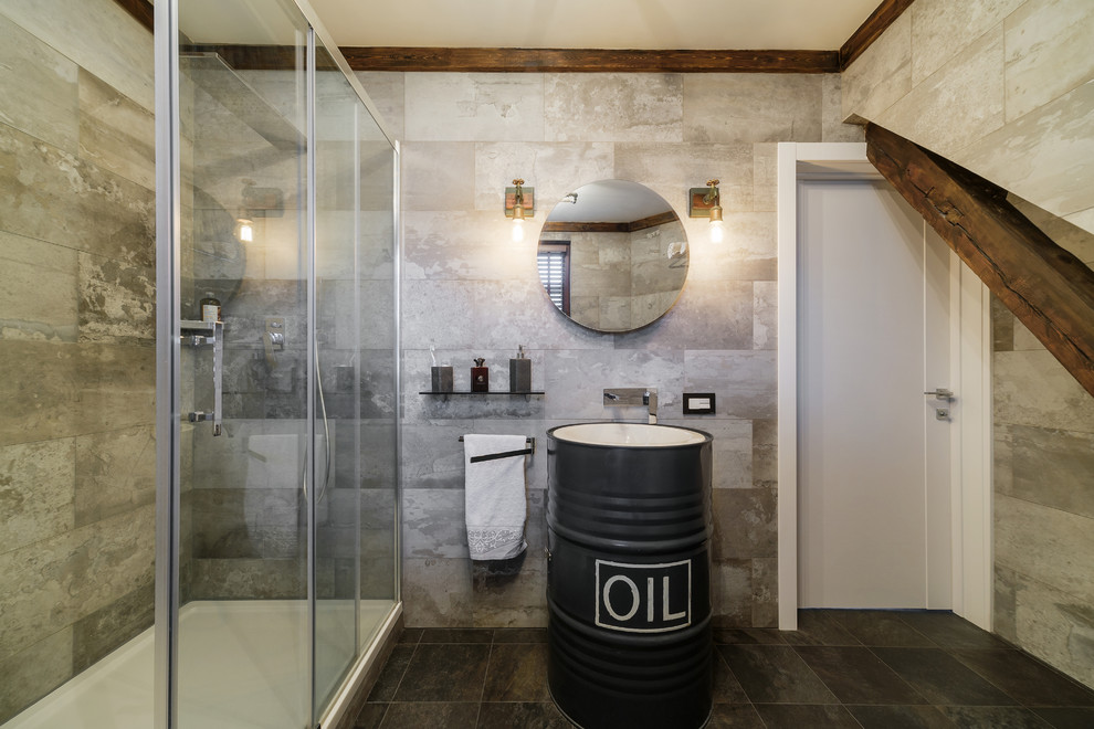 Photo of a mid-sized industrial 3/4 bathroom in Other with flat-panel cabinets, black cabinets, an alcove shower, a wall-mount toilet, gray tile, porcelain tile, grey walls, porcelain floors, a drop-in sink, grey floor and a sliding shower screen.