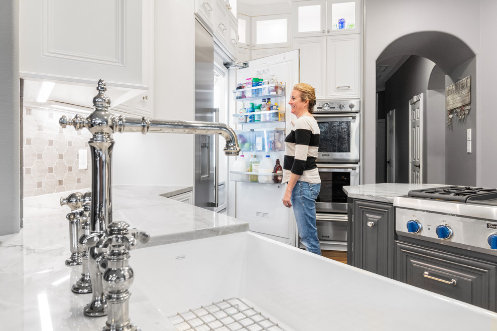 Example of a large transitional u-shaped dark wood floor and brown floor kitchen pantry design in Houston with a farmhouse sink, raised-panel cabinets, gray cabinets, quartzite countertops, gray backsplash, limestone backsplash, stainless steel appliances, a peninsula and gray countertops