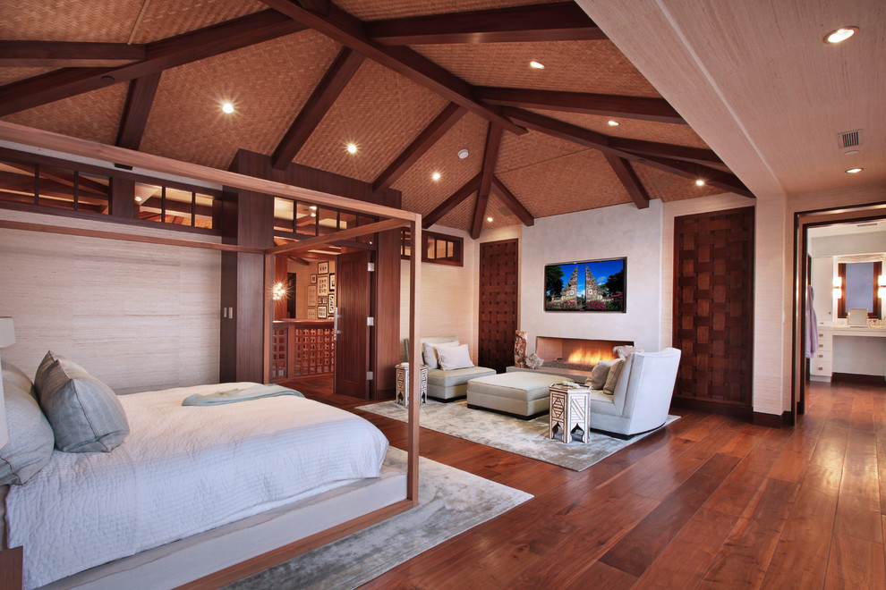 This is an example of a tropical bedroom in Orange County with beige walls, dark hardwood floors and a ribbon fireplace.