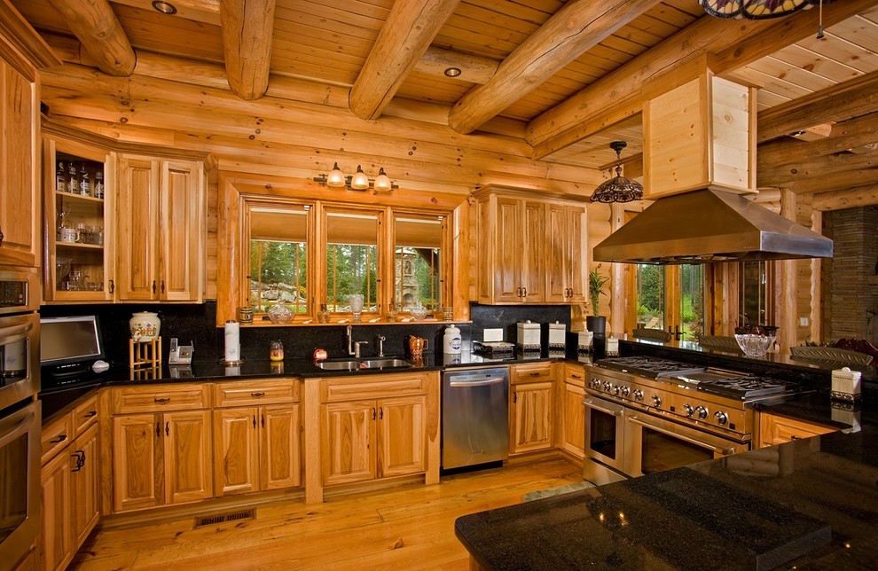 This is an example of a country u-shaped kitchen in Other with a double-bowl sink, raised-panel cabinets, medium wood cabinets, black splashback, stainless steel appliances, medium hardwood floors and black benchtop.