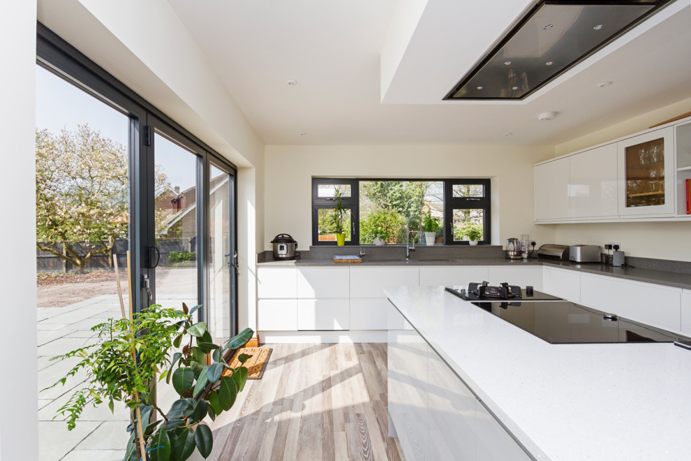 Photo of a mid-sized contemporary l-shaped open plan kitchen in West Midlands with a drop-in sink, flat-panel cabinets, white cabinets, grey splashback, panelled appliances, laminate floors, with island, grey floor and grey benchtop.