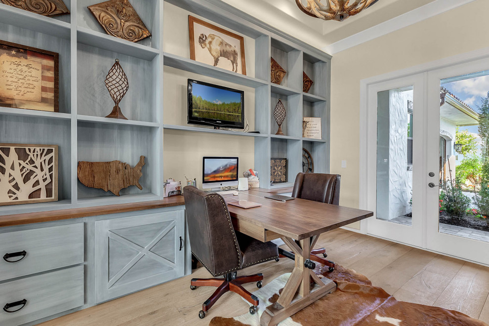 Large country home office in Orlando with a library, grey walls, light hardwood floors, a built-in desk and grey floor.
