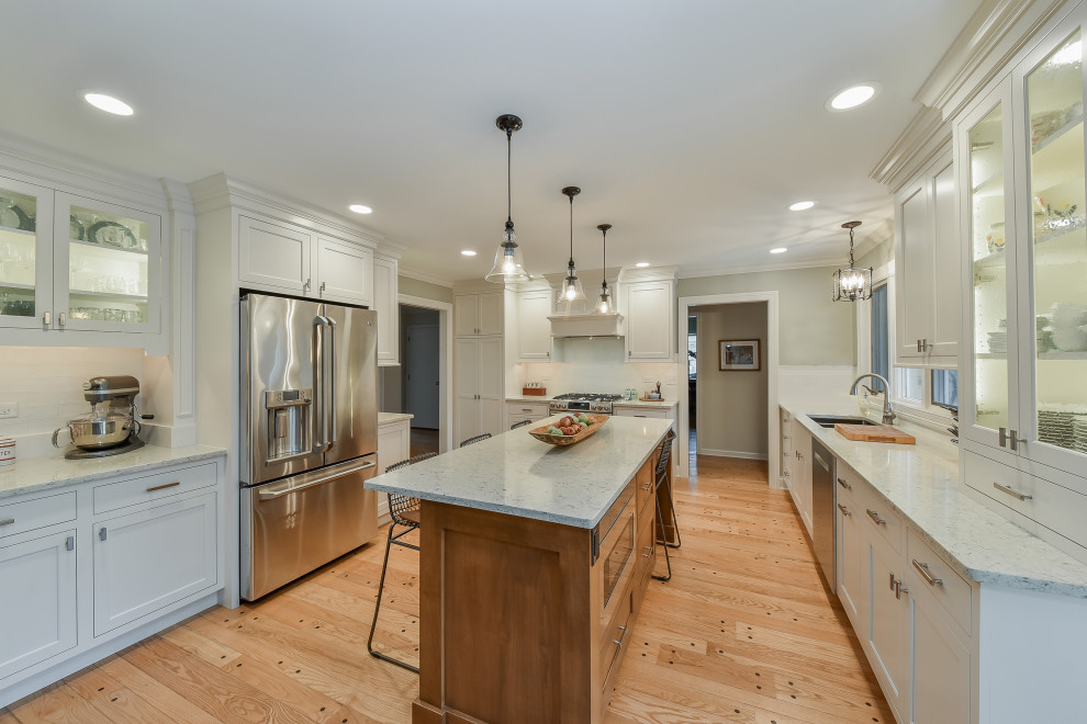 This is an example of a mid-sized transitional u-shaped eat-in kitchen in Chicago with shaker cabinets, white cabinets, quartz benchtops, white splashback, ceramic splashback, light hardwood floors, with island, yellow floor and white benchtop.