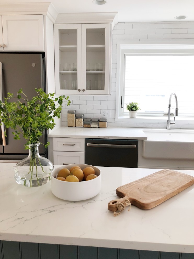 Kitchen - mid-sized transitional l-shaped light wood floor kitchen idea in Providence with a farmhouse sink, shaker cabinets, white cabinets, quartz countertops, white backsplash, ceramic backsplash, stainless steel appliances, an island and white countertops
