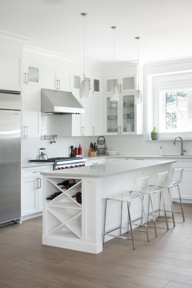 Inspiration for a modern l-shaped kitchen/diner in Vancouver with recessed-panel cabinets, white cabinets, white splashback, stainless steel appliances, laminate floors, an island, brown floors, white worktops and engineered stone countertops.