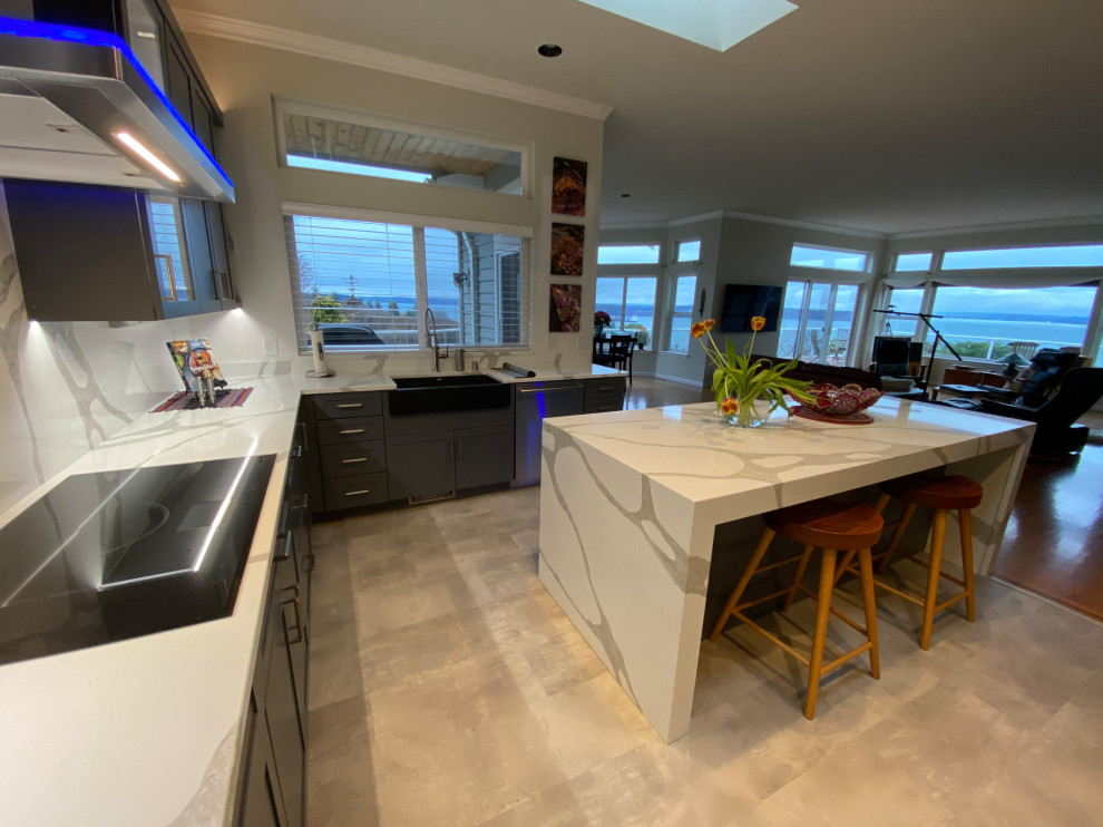 Photo of a contemporary u-shaped eat-in kitchen in San Francisco with a farmhouse sink, shaker cabinets, grey cabinets, quartz benchtops, white splashback, engineered quartz splashback, stainless steel appliances, porcelain floors, with island and white benchtop.