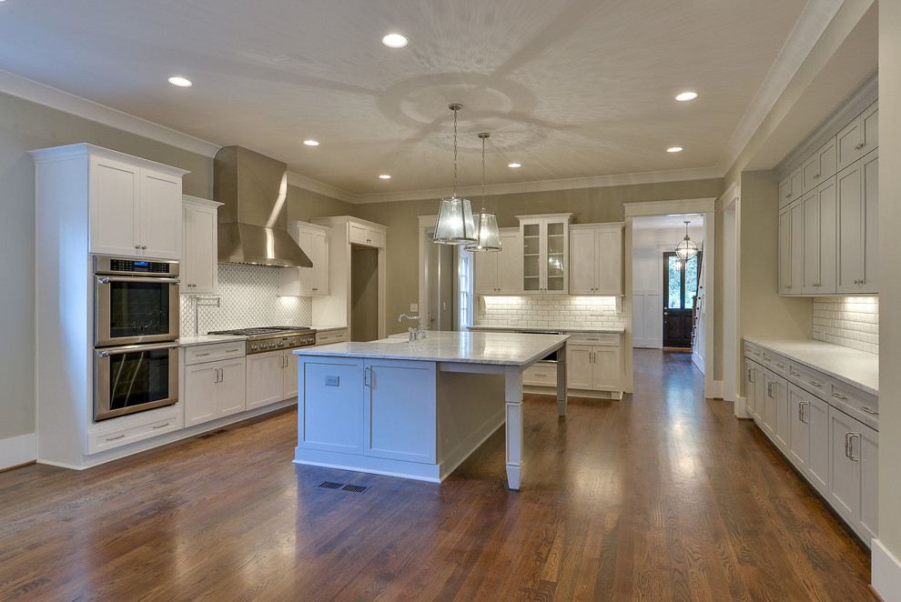 Mid-sized transitional u-shaped light wood floor and multicolored floor eat-in kitchen photo with a farmhouse sink, shaker cabinets, gray cabinets, quartz countertops, white backsplash, porcelain backsplash, stainless steel appliances, an island and gray countertops