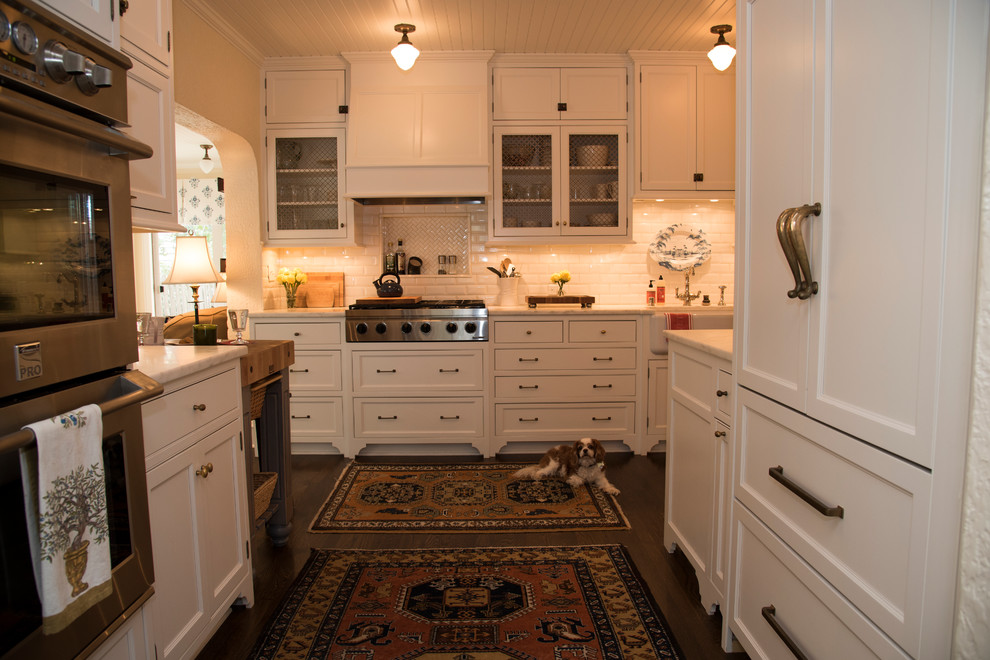 Inspiration for a mid-sized traditional l-shaped kitchen in Milwaukee with a farmhouse sink, beaded inset cabinets, white cabinets, marble benchtops, white splashback, ceramic splashback, stainless steel appliances and dark hardwood floors.