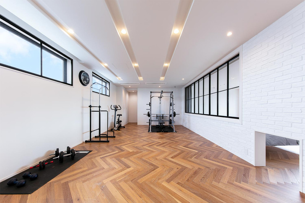 Exemple d'une salle de musculation industrielle avec un mur blanc, un sol en bois brun et un sol marron.