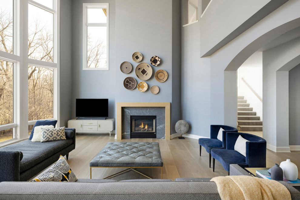 This is an example of an expansive transitional formal open concept living room in Minneapolis with grey walls, medium hardwood floors, a standard fireplace, a wood fireplace surround, a freestanding tv and brown floor.