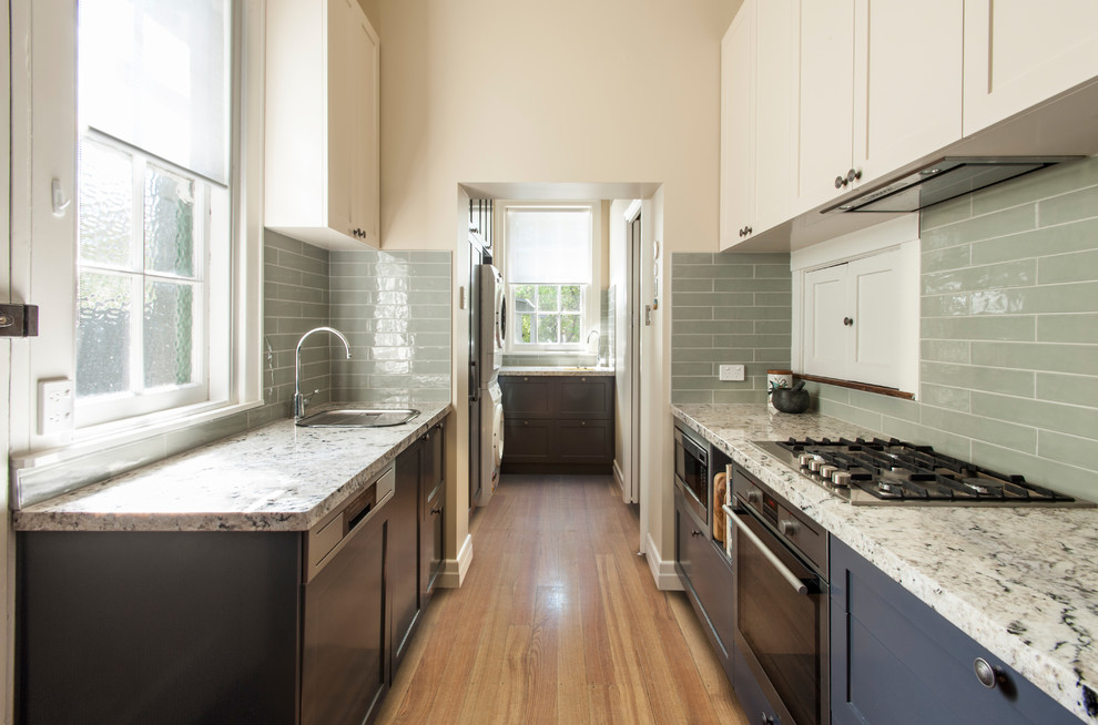 Mid-sized arts and crafts galley kitchen pantry in Melbourne with an undermount sink, recessed-panel cabinets, grey cabinets, granite benchtops, green splashback, subway tile splashback, stainless steel appliances, medium hardwood floors, no island and brown floor.