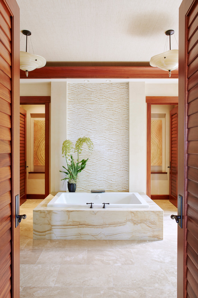 Photo of a large tropical bathroom in Hawaii with a drop-in tub and beige tile.