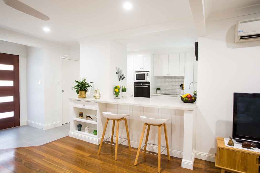 This is an example of a small traditional u-shaped kitchen pantry in Brisbane with a double-bowl sink, shaker cabinets, white cabinets, quartz benchtops, grey splashback, ceramic splashback, black appliances, porcelain floors, with island, grey floor and white benchtop.