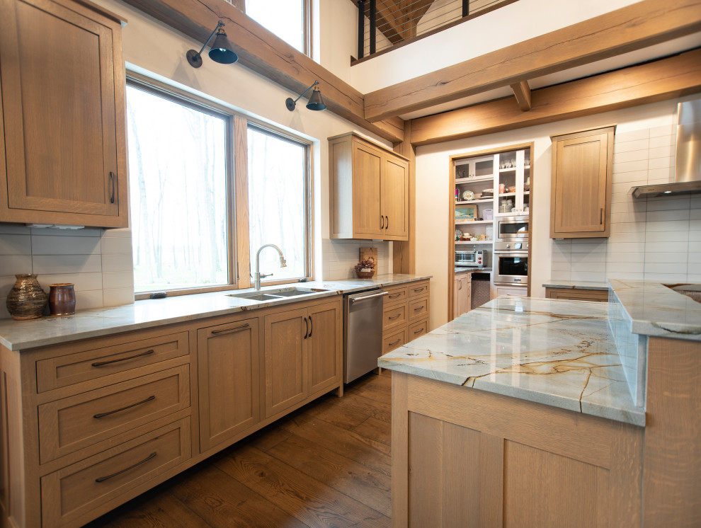 Example of a large mountain style l-shaped medium tone wood floor and exposed beam kitchen design with an undermount sink, shaker cabinets, quartz countertops, gray backsplash, ceramic backsplash, stainless steel appliances and an island