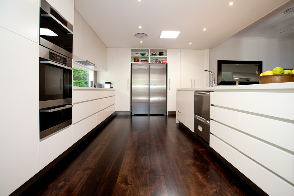 Photo of a large contemporary galley eat-in kitchen in Brisbane with a double-bowl sink, flat-panel cabinets, white cabinets, quartz benchtops, brown splashback, glass tile splashback, stainless steel appliances, with island and dark hardwood floors.