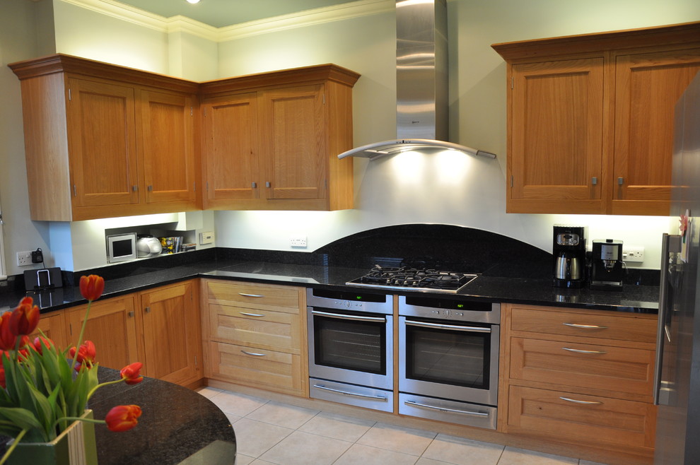 Photo of a medium sized classic u-shaped kitchen/diner in Hertfordshire with a built-in sink, recessed-panel cabinets, light wood cabinets, granite worktops, beige splashback, stainless steel appliances, ceramic flooring and an island.