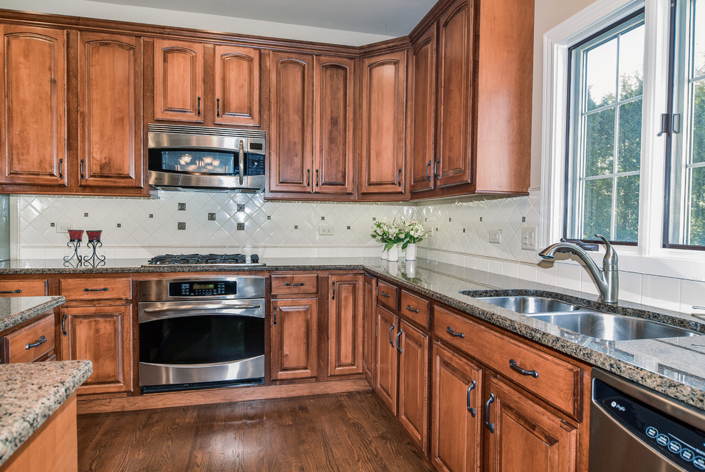 Eat-in kitchen - large transitional u-shaped medium tone wood floor eat-in kitchen idea in Chicago with a double-bowl sink, raised-panel cabinets, distressed cabinets, granite countertops, white backsplash, ceramic backsplash, stainless steel appliances and an island