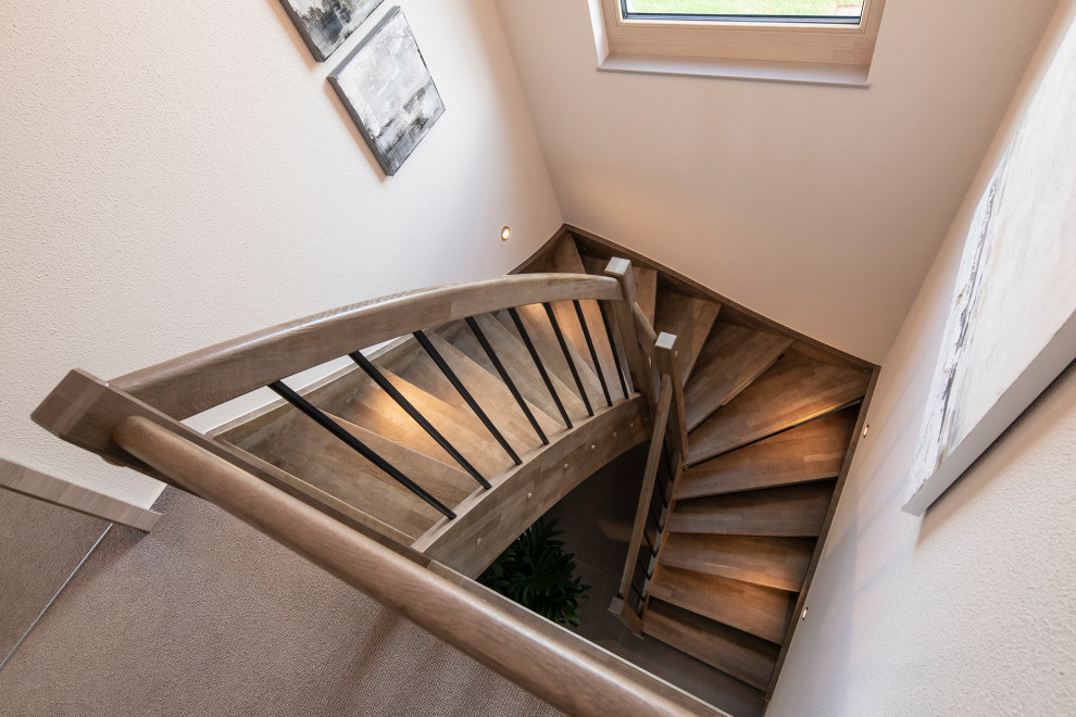 Ejemplo de escalera curva minimalista con escalones de madera y barandilla de madera