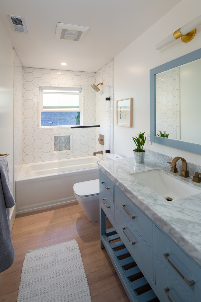 Mid-sized eclectic kids bathroom in San Francisco with flat-panel cabinets, blue cabinets, an alcove tub, white tile, white walls, light hardwood floors, an undermount sink and marble benchtops.