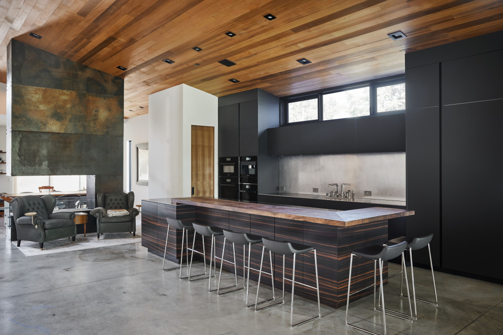 Inspiration for a large modern single-wall open plan kitchen in San Francisco with an integrated sink, flat-panel cabinets, black cabinets, stainless steel benchtops, black appliances, concrete floors and with island.