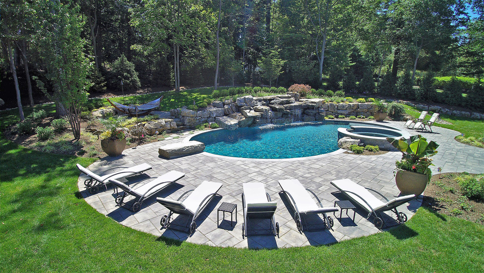 This is an example of a large tropical backyard kidney-shaped lap pool in New York with a hot tub and natural stone pavers.