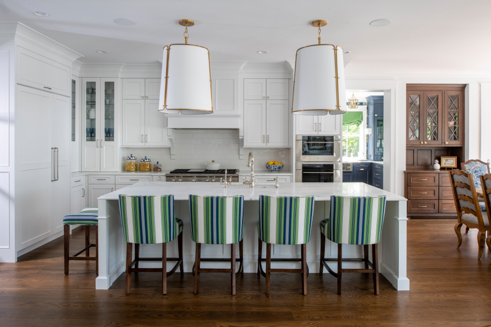 Photo of a large beach style l-shaped eat-in kitchen in Minneapolis with a farmhouse sink, recessed-panel cabinets, blue cabinets, marble benchtops, panelled appliances, medium hardwood floors, with island, brown floor and white benchtop.
