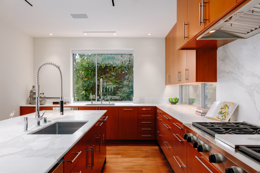Inspiration for a large contemporary u-shaped open plan kitchen in Los Angeles with an undermount sink, flat-panel cabinets, medium wood cabinets, marble benchtops, white splashback, marble splashback, stainless steel appliances, medium hardwood floors, with island, white benchtop and brown floor.