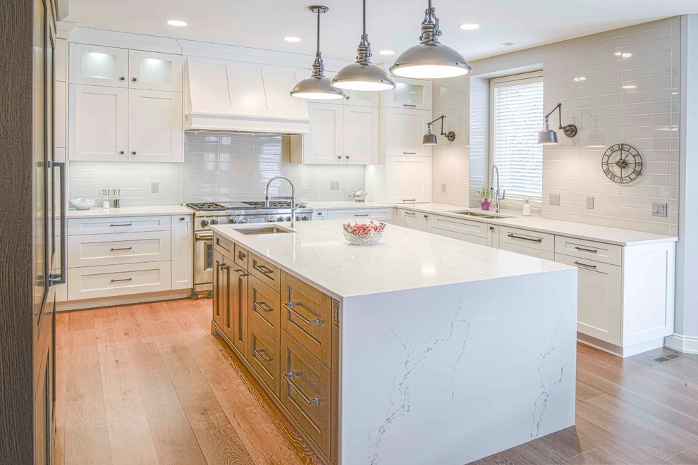 Mid-sized transitional u-shaped medium tone wood floor and brown floor kitchen photo in Calgary with an undermount sink, flat-panel cabinets, white cabinets, marble countertops, gray backsplash, ceramic backsplash, paneled appliances and an island