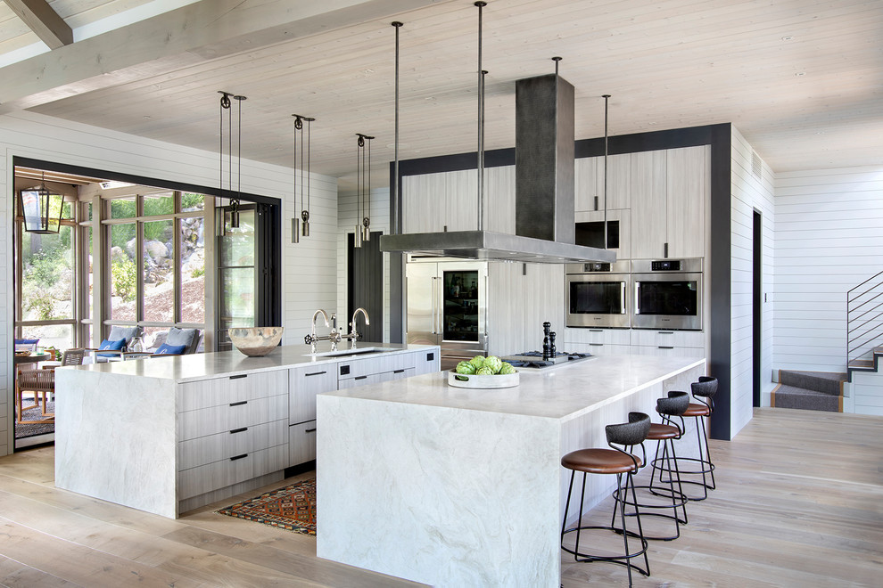 Inspiration for a country u-shaped kitchen in Other with an undermount sink, flat-panel cabinets, beige cabinets, stainless steel appliances, light hardwood floors, multiple islands, beige floor and beige benchtop.