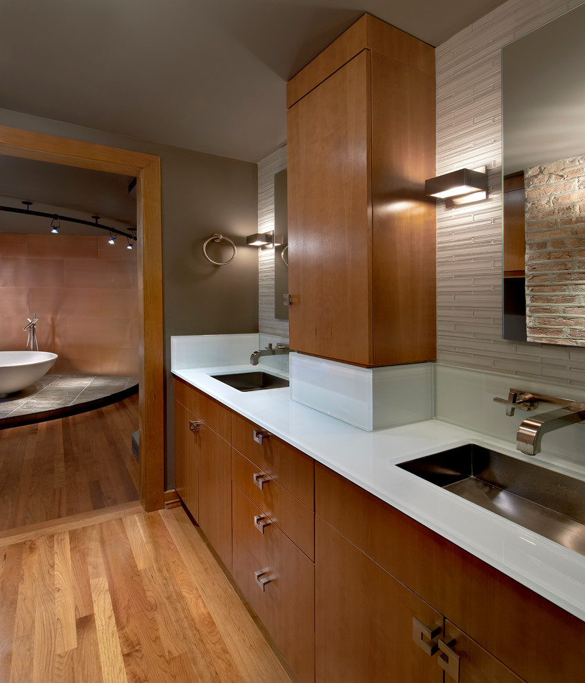 This is an example of a mid-sized contemporary master bathroom in Chicago with furniture-like cabinets, medium wood cabinets, a freestanding tub, brown walls, medium hardwood floors, glass benchtops and an undermount sink.