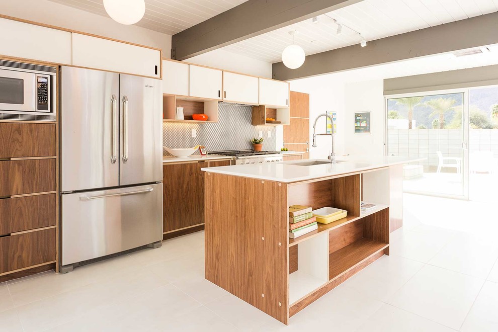 This is an example of a mid-sized midcentury galley open plan kitchen in Los Angeles with an undermount sink, flat-panel cabinets, white cabinets, stainless steel appliances, with island, white floor, quartz benchtops, grey splashback, mosaic tile splashback and porcelain floors.