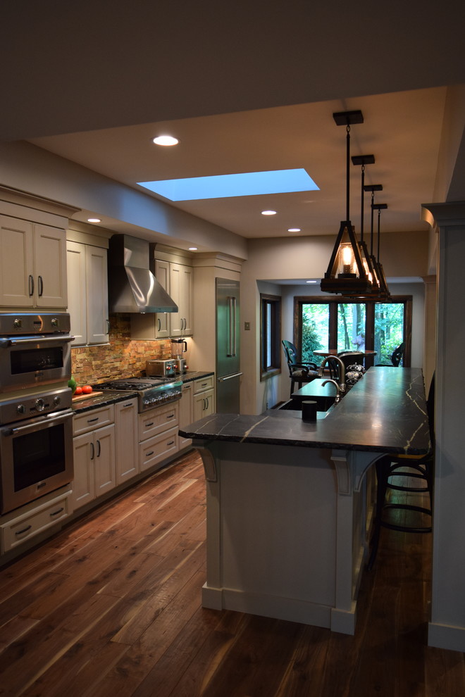 Large transitional galley medium tone wood floor kitchen photo with an undermount sink, recessed-panel cabinets, white cabinets, quartz countertops, multicolored backsplash, stone slab backsplash, stainless steel appliances and an island