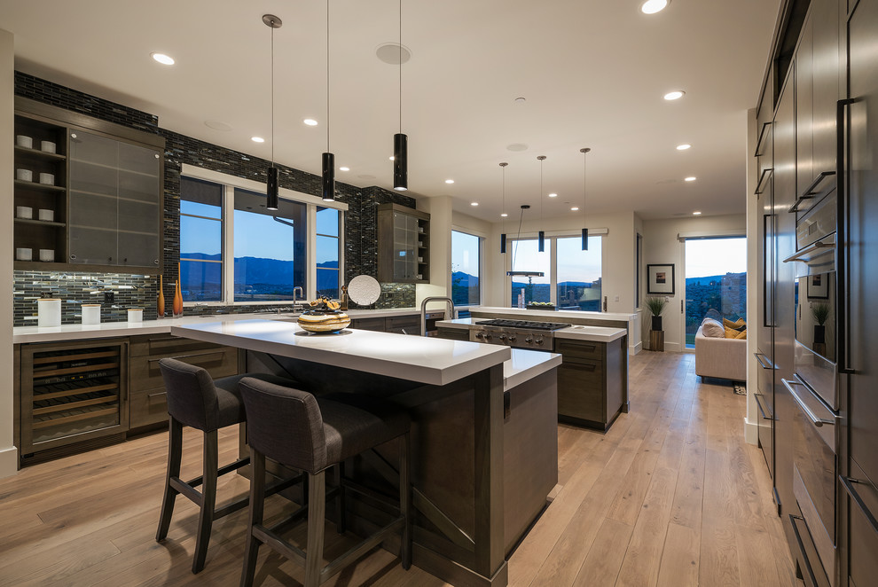 Design ideas for a mid-sized contemporary u-shaped open plan kitchen in Salt Lake City with an undermount sink, flat-panel cabinets, dark wood cabinets, quartzite benchtops, black splashback, glass tile splashback, stainless steel appliances, light hardwood floors and multiple islands.