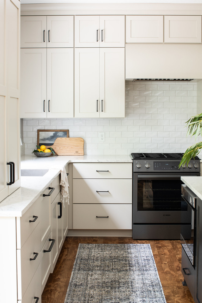Inspiration for a mid-sized transitional u-shaped medium tone wood floor and brown floor eat-in kitchen remodel with an undermount sink, shaker cabinets, white cabinets, quartz countertops, white backsplash, subway tile backsplash, black appliances, an island and white countertops