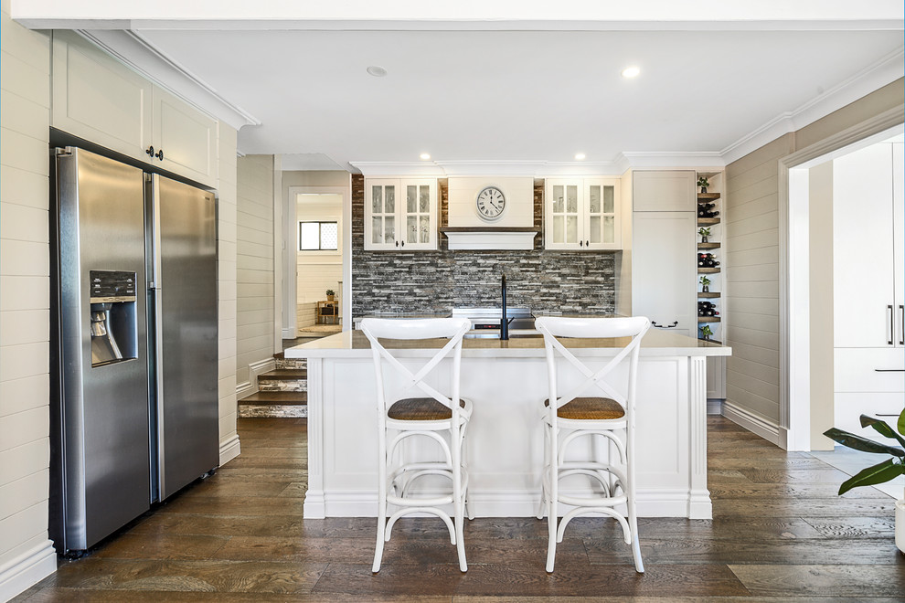 Design ideas for a beach style kitchen in Gold Coast - Tweed with glass-front cabinets, white cabinets, multi-coloured splashback, stainless steel appliances, dark hardwood floors and with island.