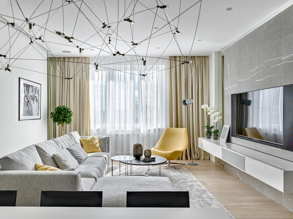 This is an example of a contemporary formal open concept living room in Moscow with white walls, light hardwood floors and a wall-mounted tv.