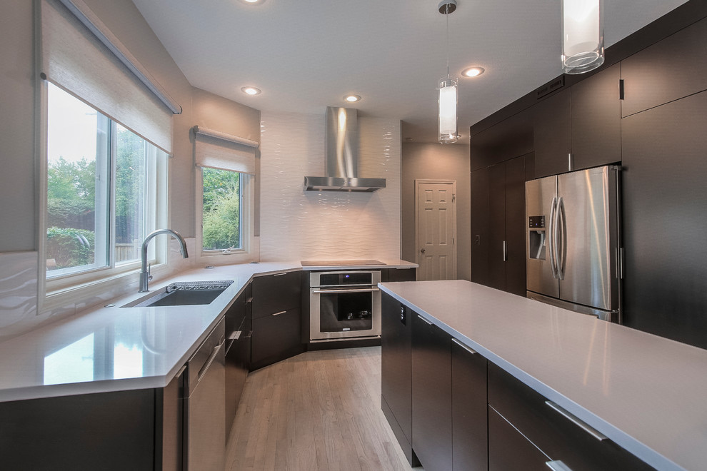 Photo of a large contemporary u-shaped open plan kitchen in Kansas City with an undermount sink, flat-panel cabinets, dark wood cabinets, quartzite benchtops, white splashback, ceramic splashback, stainless steel appliances, light hardwood floors and with island.