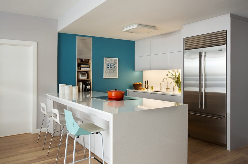Inspiration for a mid-sized contemporary single-wall eat-in kitchen in Boston with an undermount sink, flat-panel cabinets, white cabinets, quartz benchtops, white splashback, stainless steel appliances, light hardwood floors and with island.