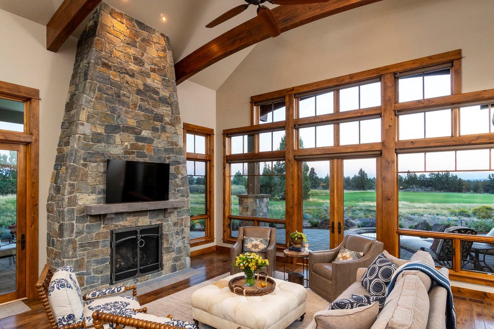 Inspiration for a large country open concept family room in Other with beige walls, a standard fireplace, a stone fireplace surround, a wall-mounted tv, dark hardwood floors and brown floor.