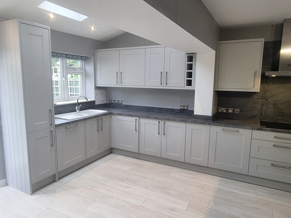 Photo of a mid-sized modern u-shaped open plan kitchen in London with a single-bowl sink, shaker cabinets, white cabinets, laminate benchtops, grey splashback, panelled appliances, laminate floors and grey benchtop.