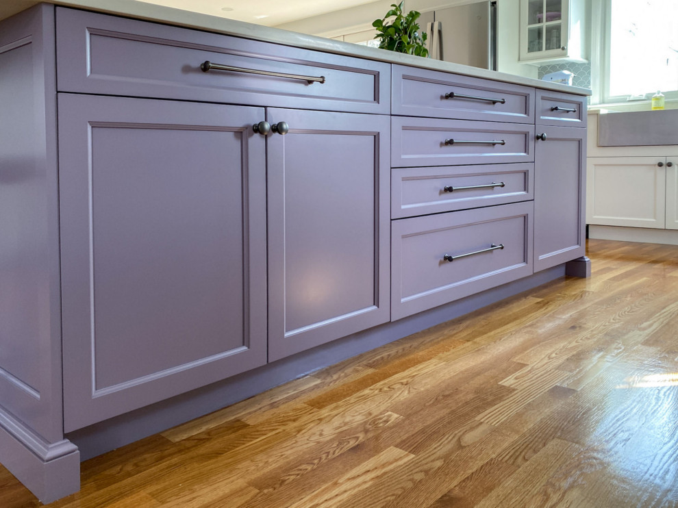 Design ideas for a transitional l-shaped kitchen in Boston with a farmhouse sink, shaker cabinets, purple cabinets, quartz benchtops, grey splashback, ceramic splashback, stainless steel appliances, light hardwood floors, with island and white benchtop.