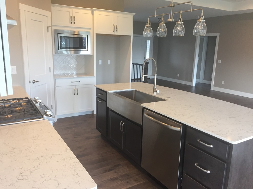 Mid-sized transitional l-shaped dark wood floor and brown floor kitchen photo in Cedar Rapids with a farmhouse sink, shaker cabinets, white cabinets, quartz countertops, white backsplash, ceramic backsplash, stainless steel appliances, an island and white countertops