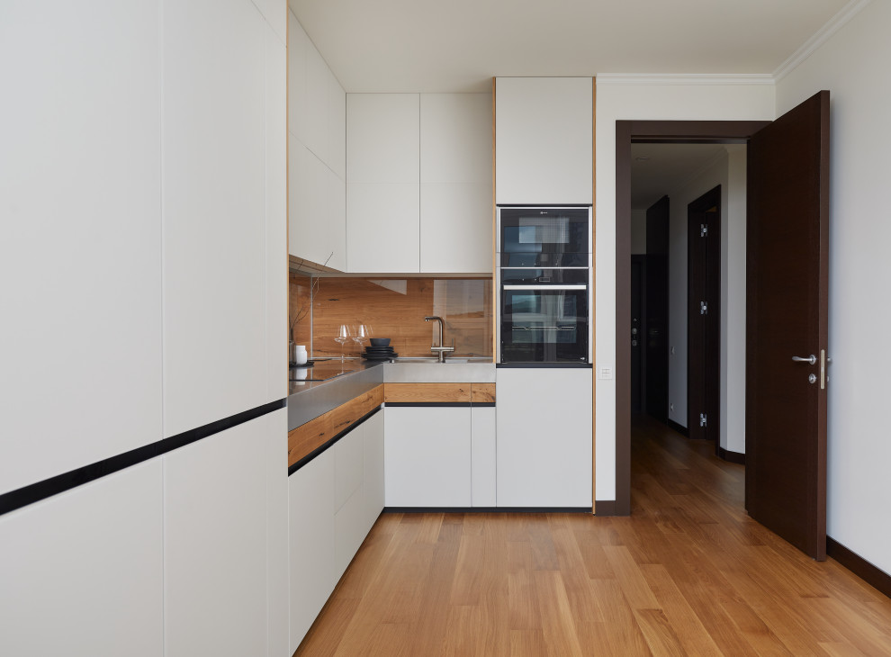 Photo of a mid-sized l-shaped eat-in kitchen in Moscow with a double-bowl sink, white cabinets, stainless steel benchtops, brown splashback, timber splashback, panelled appliances, no island and grey benchtop.