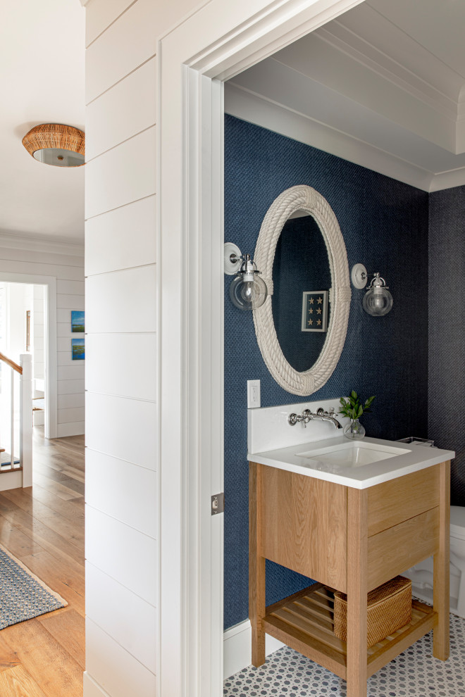 Cette image montre un petit WC et toilettes marin en bois clair avec un placard en trompe-l'oeil, un sol en carrelage de céramique, un lavabo encastré, un plan de toilette en quartz, un sol bleu, un plan de toilette blanc, meuble-lavabo encastré et du papier peint.