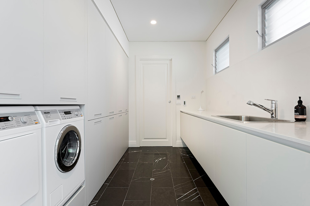 Design ideas for a large contemporary galley dedicated laundry room in Perth with a single-bowl sink, flat-panel cabinets, white cabinets, quartz benchtops, white splashback, glass sheet splashback, white walls, marble floors, a side-by-side washer and dryer, grey floor and white benchtop.