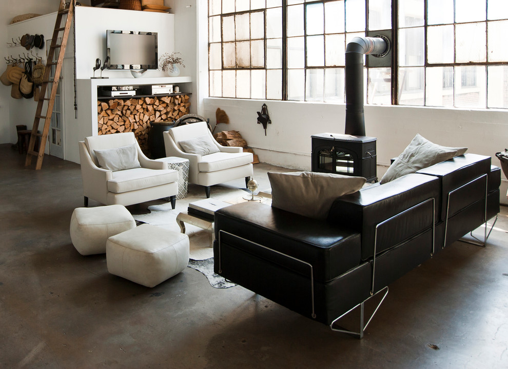 This is an example of an industrial open concept living room in New York with concrete floors and a wood stove.