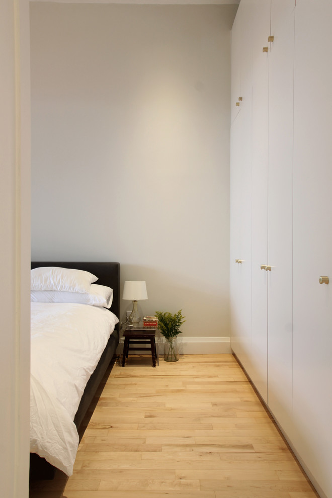 Photo of a small modern bedroom in New York with white walls and light hardwood floors.