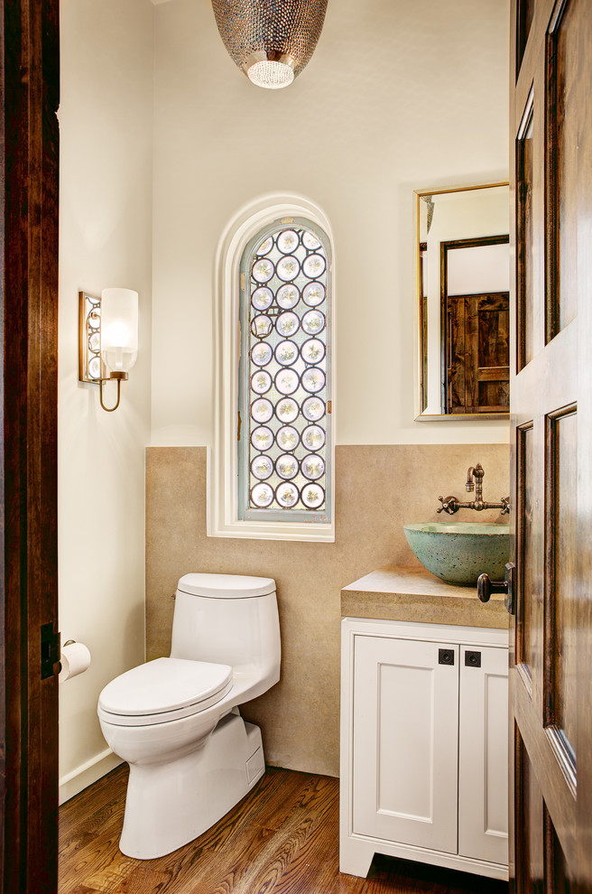 This is an example of a small mediterranean powder room in Dallas with a vessel sink, beaded inset cabinets, white cabinets, limestone benchtops, a one-piece toilet, beige tile, white walls, medium hardwood floors and limestone.