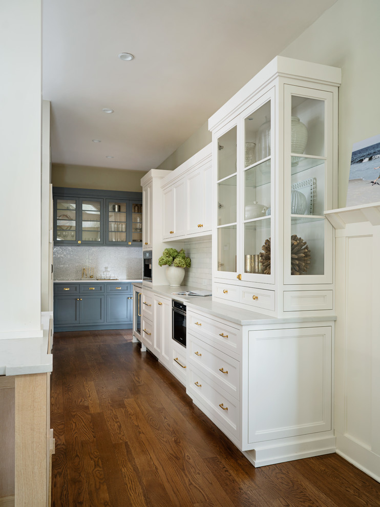 Photo of a large transitional kitchen in New York with a farmhouse sink, beaded inset cabinets, light wood cabinets, white splashback, stainless steel appliances, medium hardwood floors, with island and white benchtop.