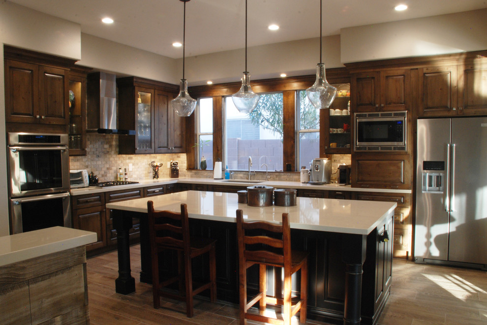 Inspiration for a mid-sized rustic l-shaped porcelain tile eat-in kitchen remodel in Phoenix with an undermount sink, raised-panel cabinets, distressed cabinets, quartzite countertops, brown backsplash, mosaic tile backsplash, stainless steel appliances and an island
